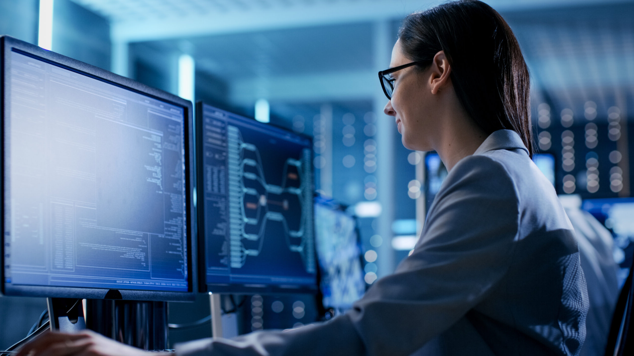 Close-up Shot of Female IT Engineer Working in Monitoring Room. She Works with Multiple Displays.
